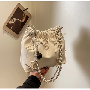 Détail du sac seau crème avec nœud décoratif et bandoulière en chaîne argentée élégante