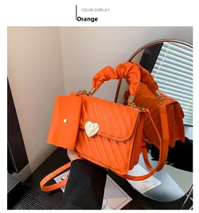 Detail of orange quilted PU leather handbag with gold heart buckle and matching mini pouch