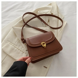 Detail of caramel leather shoulder bag with gold double-ring buckle on a beige blazer