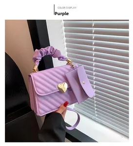 Close-up of purple quilted handbag featuring a gold heart lock and ruffled handle
