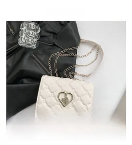 Detail of white quilted crossbody bag with heart-shaped metal twist lock and chain strap