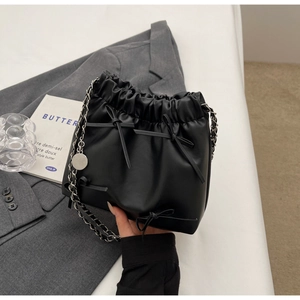 Détail du sac seau noir avec nœud décoratif, cordon de serrage et bandoulière chaîne