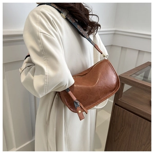 Détail d'un sac demi-lune en cuir marron avec une large bandoulière en tissu à motifs