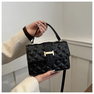 Detail of black quilted leather handbag with gold bar buckle and crossbody strap