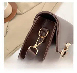 Detail showing the polished golden metal hook and precise stitching on dark brown leather bag