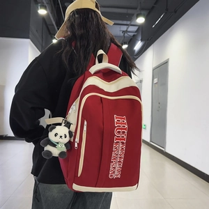 Red nylon backpack for students with ivory trim and panda pendant in campus hallway