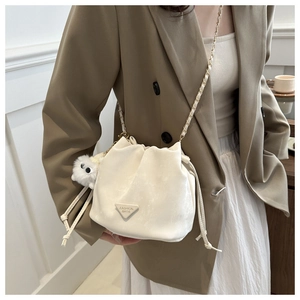 Close-up of white velvet drawstring bucket bag with gold chain and plush ball pendant