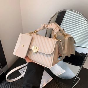 Quilted beige handbag with a gold heart clasp and pleated handle in soft lighting