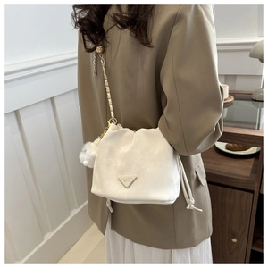 White drawstring bucket bag with gold chain strap and plush pompom on a model