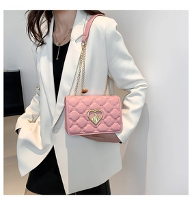 Detail of pink quilted handbag with gold heart buckle and chain strap on a white blazer