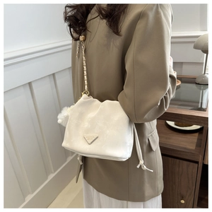 Detail of white drawstring bucket bag featuring a gold chain strap and plush ball charm