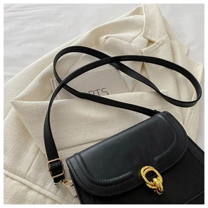 Detail of black leather crossbody bag featuring gold hardware on a beige blazer