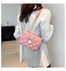 Pink quilted crossbody bag with gold heart lock shown on model wearing white blazer