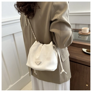 Close-up of a white velvet drawstring bucket bag with a golden chain strap on a model