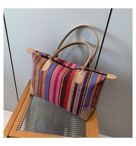 Detail of colorful striped woven tote bag with khaki leather handles on wooden stool