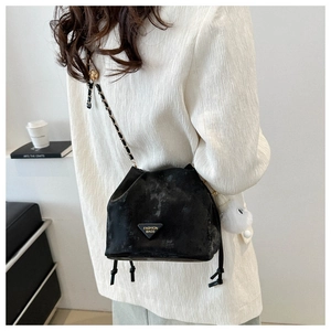 Detail of black suede bucket bag with metal chain strap and white plush pompom charm