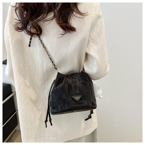 Detail of a vintage black bucket bag with a metal triangle logo and woven chain strap