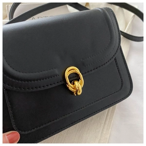 Close-up of black leather crossbody bag featuring a shiny gold interlocking hardware buckle