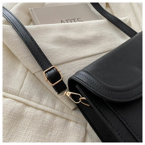 Detail view of black faux leather bag showing golden metal buckle and curved side stitching