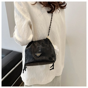 Detail of black bucket bag with triangular metal logo and plush white ball charm