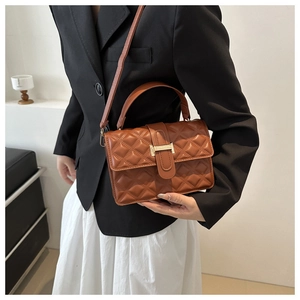 Close-up of brown quilted handbag with gold clasp and adjustable shoulder strap worn by model