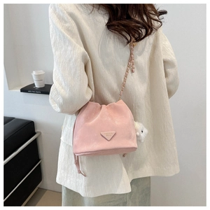 Pink bucket bag with chain strap and white plush bear charm shown in a lifestyle view