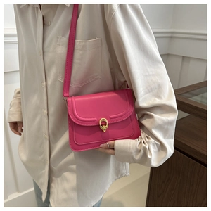 Model wearing a rose pink leather crossbody bag with a gold oval metal clasp
