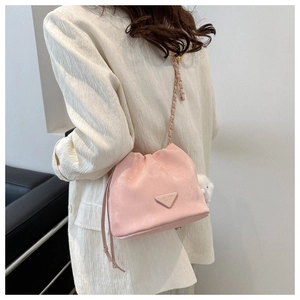 Detail of pink drawstring bucket bag featuring a woven chain strap and fashion logo plate