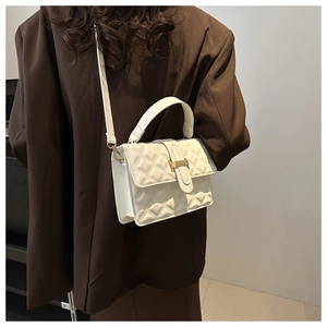 White quilted crossbody bag with gold buckle worn on a shoulder over a brown blazer
