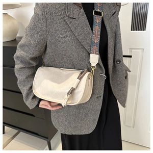 Détail d'un sac bandoulière crème avec sangle ethnique et pompon sur une veste grise