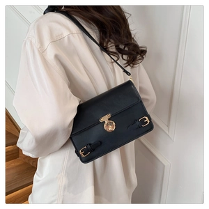 Detail of a retro black leather shoulder bag with a round gold buckle on a white shirt