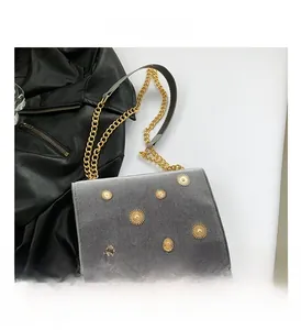 Vue macro d'un sac en velours gris avec rivets soleil dorés et bandoulière chaîne