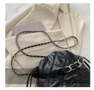 Detail shot of black quilted faux leather crossbody bag with silver chain strap on beige blazer