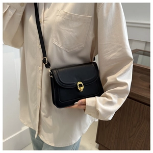 Detailed close-up of a black leather crossbody bag with a golden interlocking buckle clasp