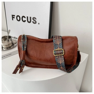 Détail du sac cylindrique en similicuir marron avec bandoulière tissée géométrique colorée