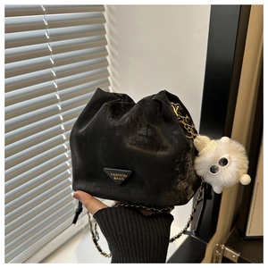 Detail of black drawstring bucket bag with gold chain strap and plush monster charm