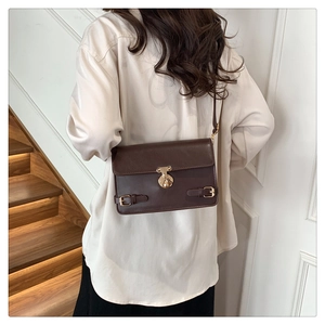 Detail of dark brown leather crossbody bag with vintage gold buckle on a white shirt