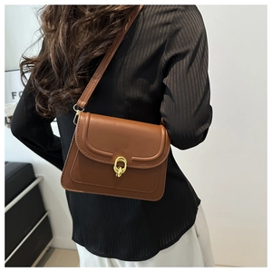 Detailed view of brown leather crossbody bag featuring a shiny gold double-ring clasp