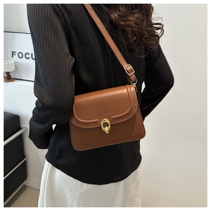 Close-up of brown leather crossbody bag with golden dual-ring clasp and stitching