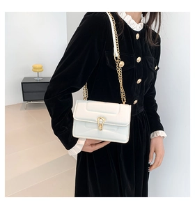 Détail du petit sac blanc brillant avec chaîne dorée et boucle en U sur une robe noire
