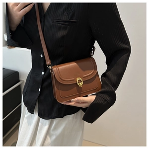 Brown leather crossbody bag with gold interlocking buckle shown on model in minimal interior