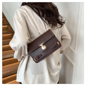 Detail of dark brown leather crossbody bag with golden buckle on a white shirt model