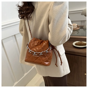 Detail view of brown quilted bucket bag with silver chain strap on a chic white blazer