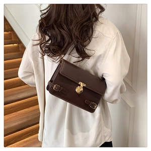 Detail of vintage brown leather satchel featuring a golden circular lock and decorative straps
