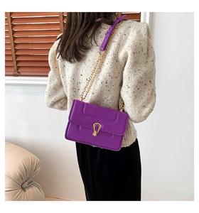 Détail du sac à bandoulière violet avec chaîne dorée porté sur un élégant pull en tweed beige