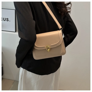 Detail of apricot crossbody bag with golden double-ring lock on a minimalist outfit