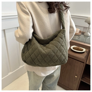Deep green quilted corduroy hobo bag shown on shoulder in a minimalist indoor setting