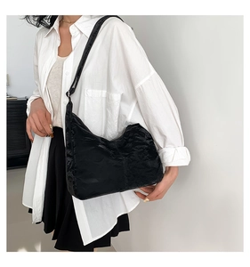 Detail of minimalist black pleated hobo bag showing glossy texture and shoulder carry style