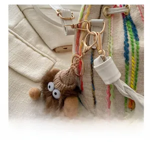 Detailed macro view of a brown plush monster charm with eyes on a beige woven bucket bag