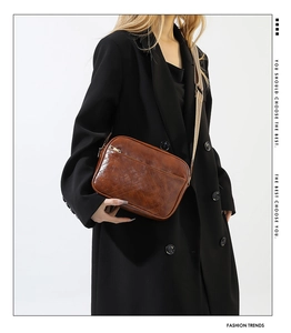 Detail of V-quilted brown leather crossbody bag with chic woven strap and metallic zipper